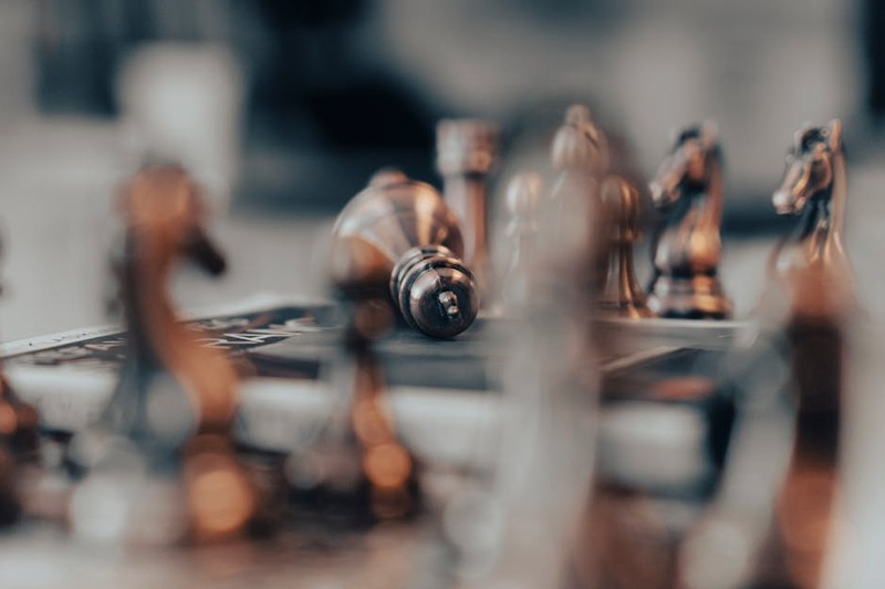 A focused artistic close-up of chess pieces on a board, featuring a fallen king, captured with shall
