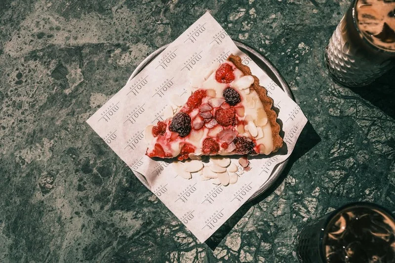 A delicate berry tart with raspberries and blueberries next to a cup of light roast coffee