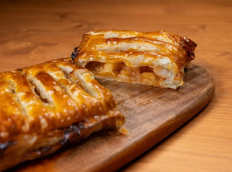 A slice of warm apple strudel with vanilla sauce next to a cup of medium roasted coffee