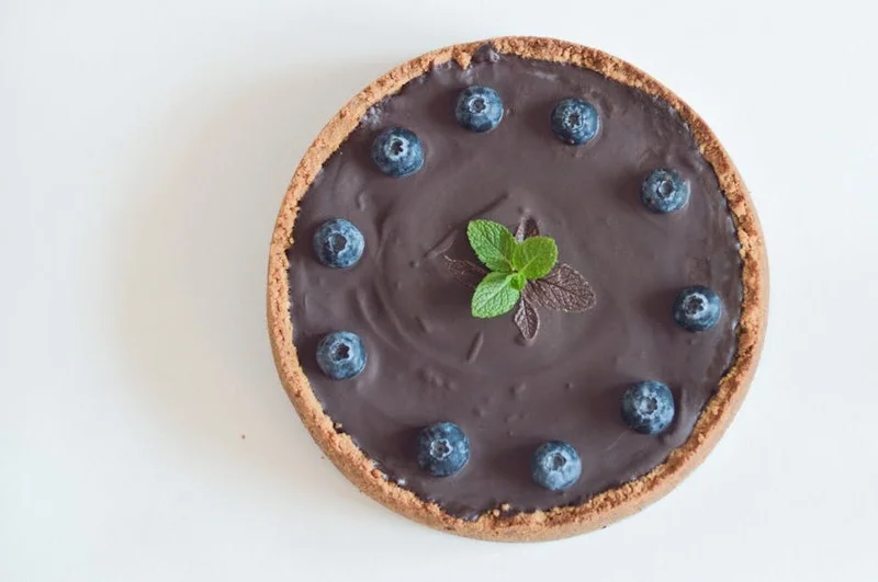 Decadent vegan chocolate avocado tart with a vibrant raspberry coulis, elegantly presented