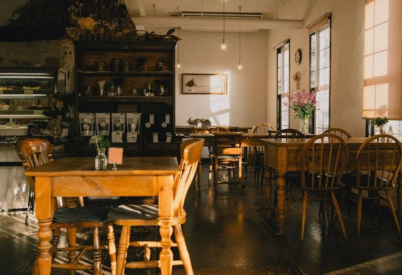 Gemütliches Interieur eines traditionellen deutschen Cafés mit Holztischen und Vintage-Stühlen, Sonnenlicht strömt durch die Fenster