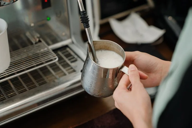 Close-up of a barista steaming milk, showing the correct angle of the wand in the pitcher for optimal microfoam
