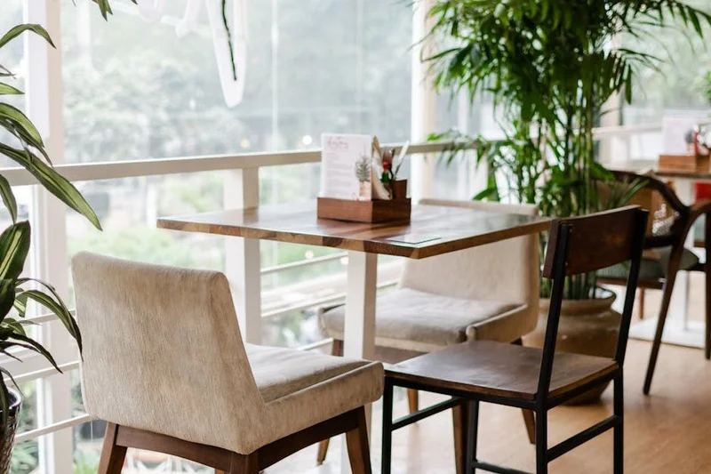 Modernes Café-Interieur mit vielen grünen Pflanzen, hellem Tageslicht und minimalistischen Holzmöbeln, eine geschäftige Atmosphäre