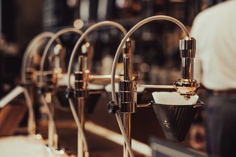 Industriell-schickes Café-Interieur mit sichtbarer Kaffeeröstausrüstung, Kupferakzenten und Baristas, die Spezialitätenkaffee zubereiten