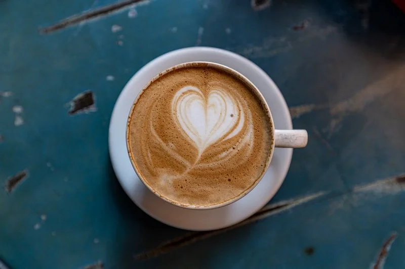 A perfectly formed latte art heart design on the surface of a cappuccino in a white ceramic cup