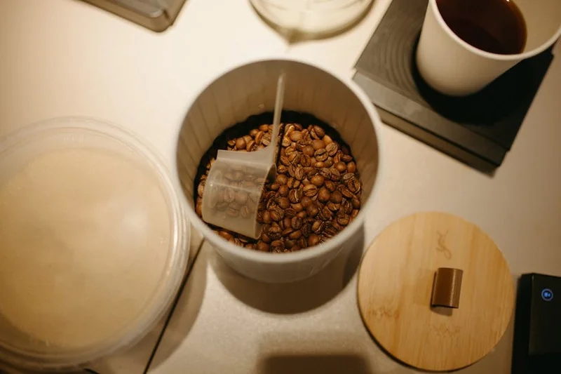 A dark, opaque, airtight container designed for storing coffee beans, placed on a clean kitchen counter